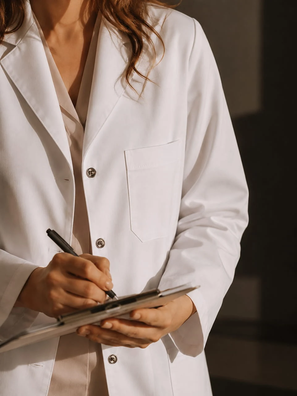 A clinician in a white coat writing on a clipboard.