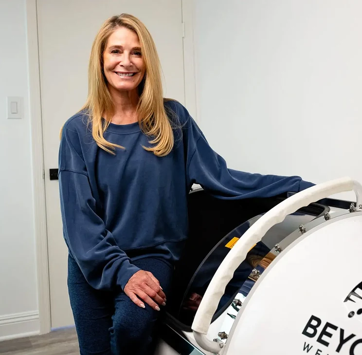 Lisa, a Beyond Wellness member, standing beside the hyperbaric chamber.