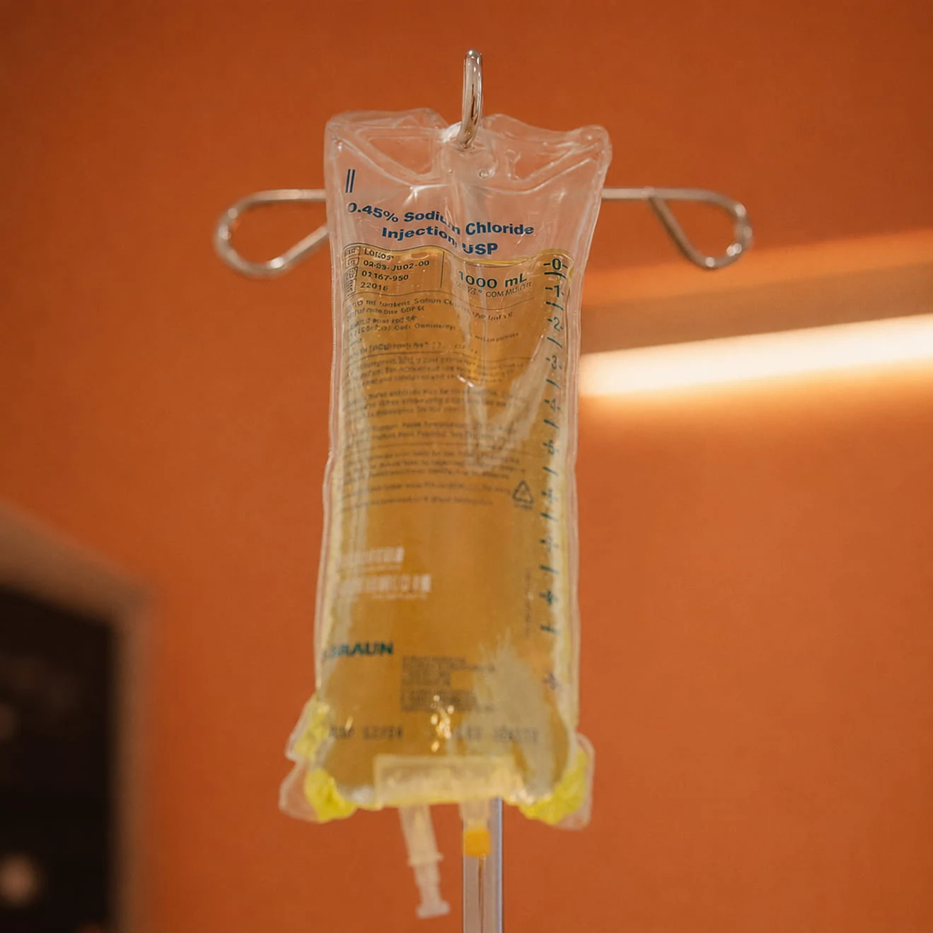 An IV bag hanging from its stand against a warm terracotta wall.