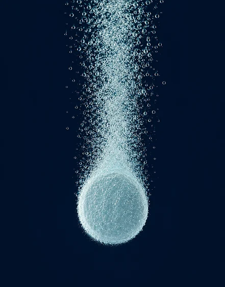 A single oral peptide capsule dissolving in water, seen in macro.